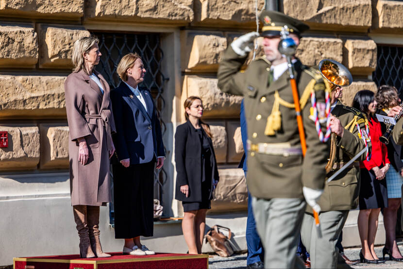 Ministers Ollongren en Jana Černochová staan op een podium terwijl saluerende militairen voorbij lopen.